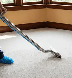 Steam carpet cleaning technician using a hot-water extraction wand on a residential carpet, wearing blue protective shoe covers Erie, PA.