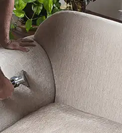 Professional upholstery cleaner deep-cleaning a fabric sofa with a handheld extraction tool and hose Erie, PA.