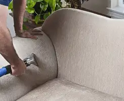 Professional upholstery cleaner deep-cleaning a fabric sofa with a handheld extraction tool and hose in Erie, PA.